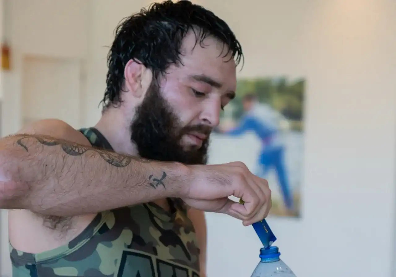 Sporter in camo-shirt voegt elektrolyten poeder toe aan fles water na intensieve training