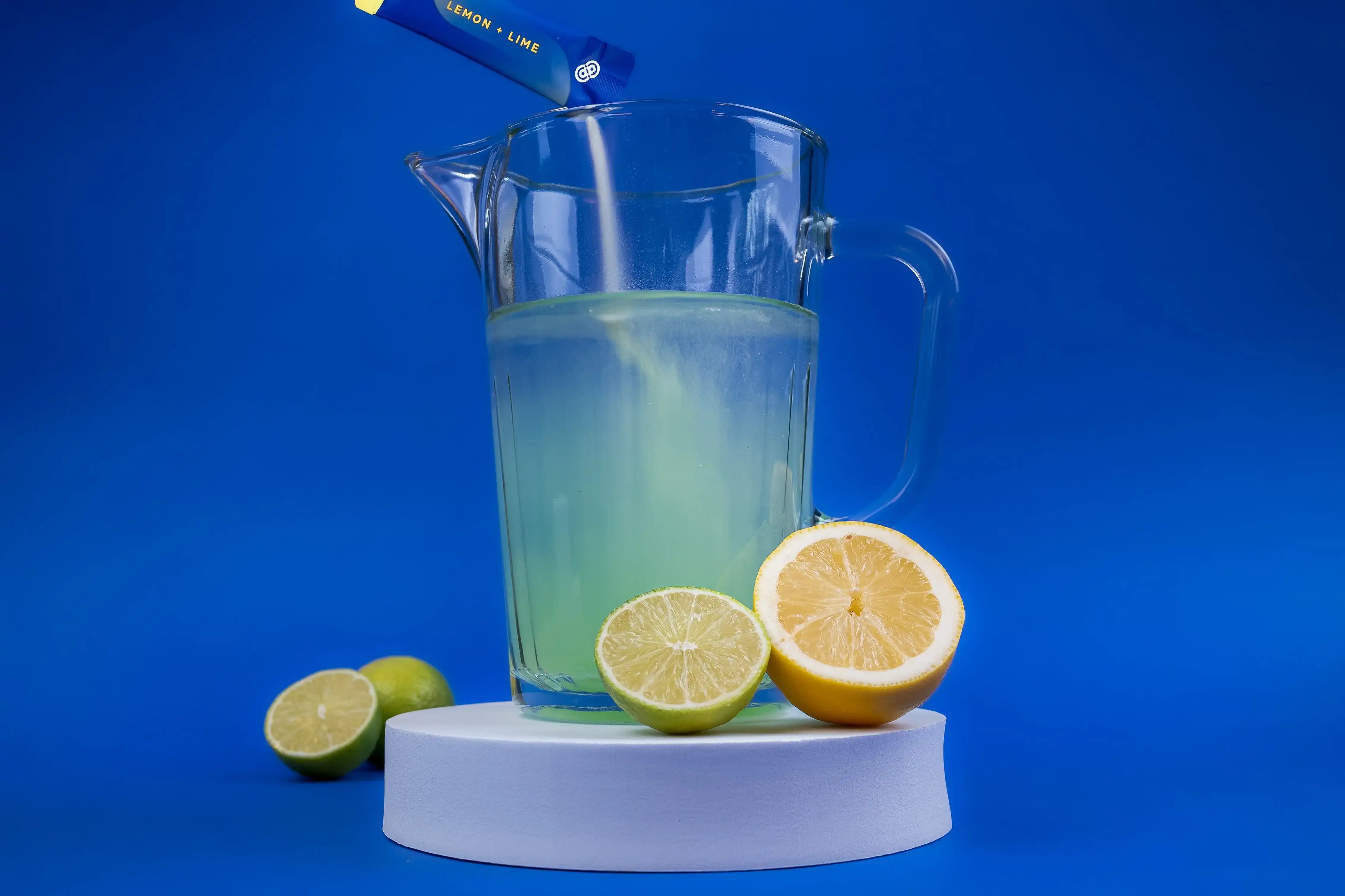 Glazen kan met elektrolyten drank in lemon-lime smaak en citroenen op blauwe achtergrond