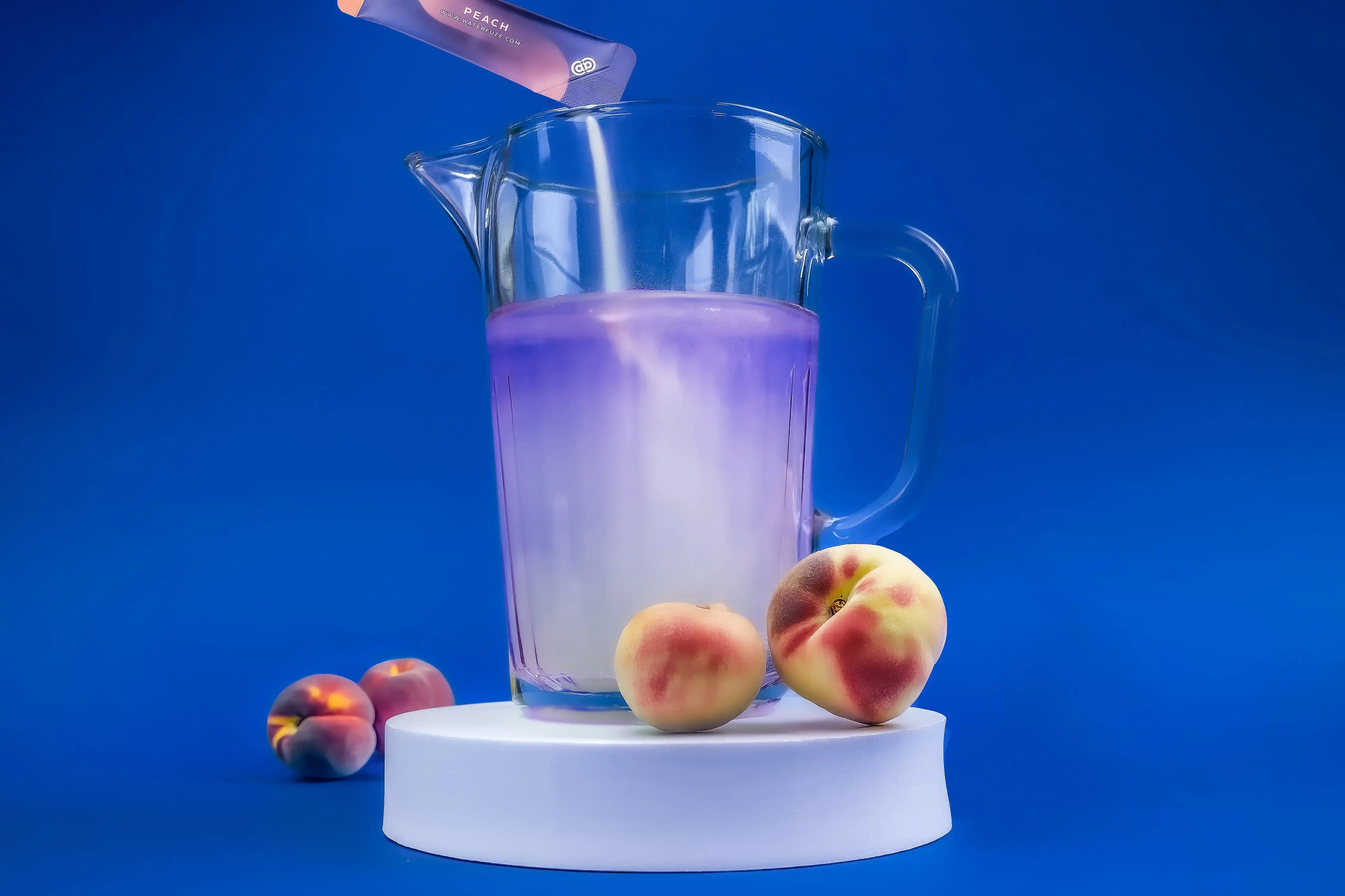 Glazen kan met paarse elektrolyten drank en perziksmaak poeder tegen blauwe achtergrond, omringd door verse perziken