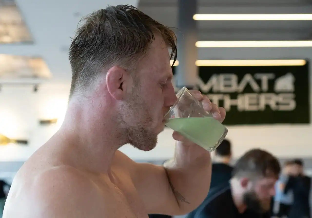 Sporter drinkt groene elektrolyten drank na training in gym omgeving voor optimale hydratatie
