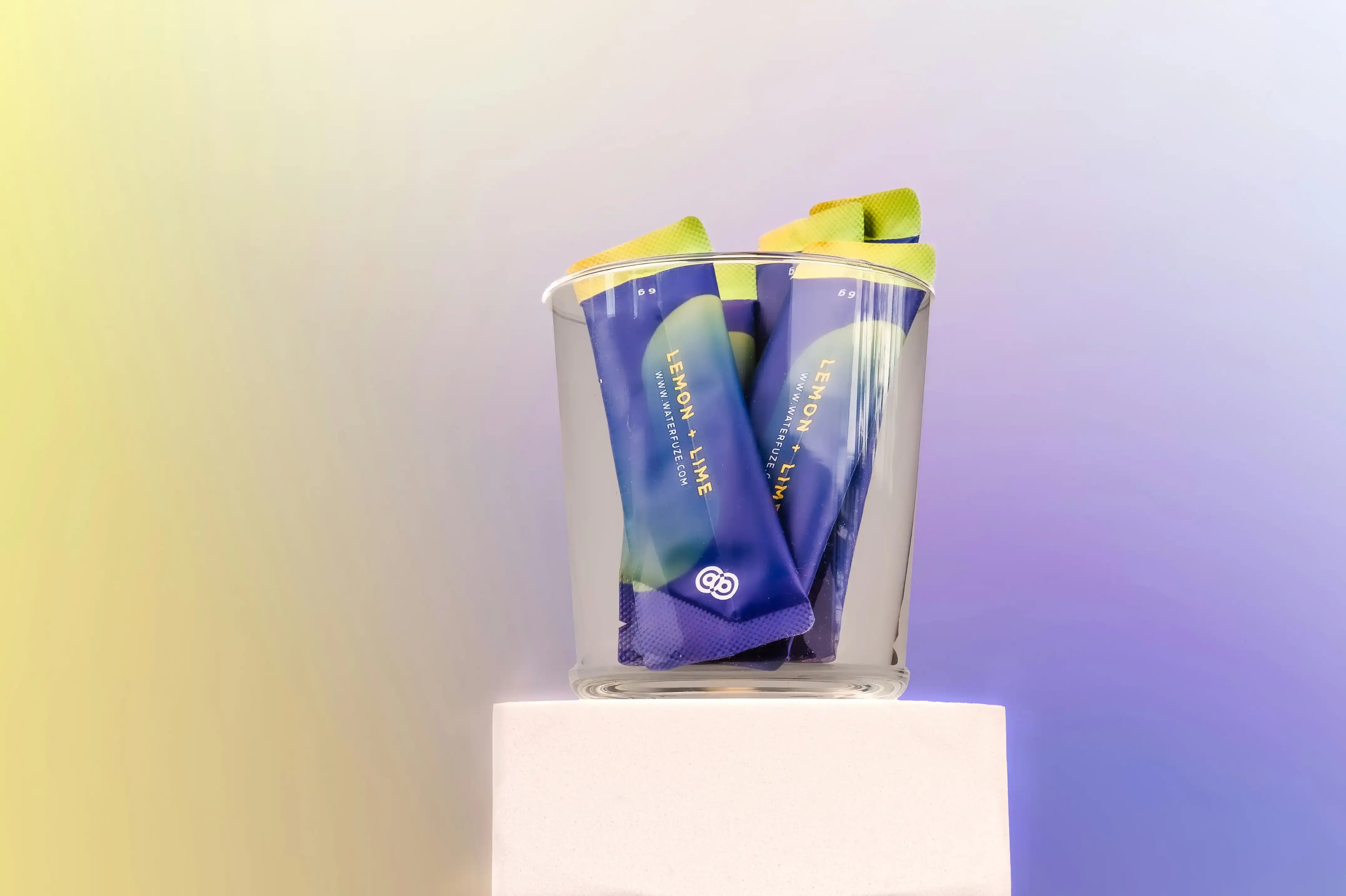 Glas gevuld met lemon-lime elektrolyten sticks van Waterfuze tegen zachte pastel achtergrond