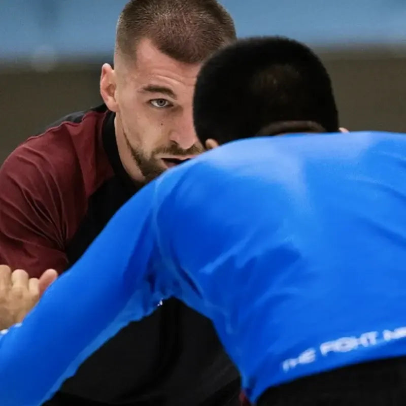 Twee mannen geconcentreerd in een worstel- of grapplingpositie tijdens een intense trainingssessie.
