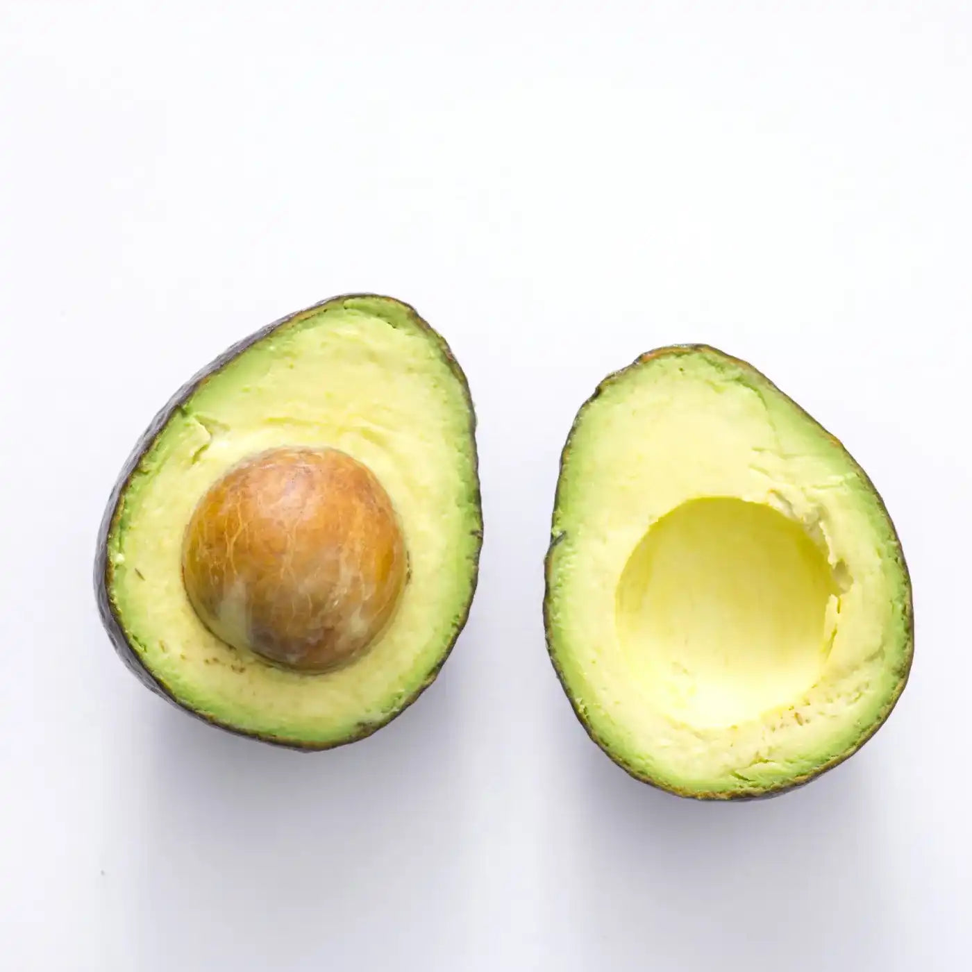 Een doormidden gesneden avocado met pit, op een witte achtergrond