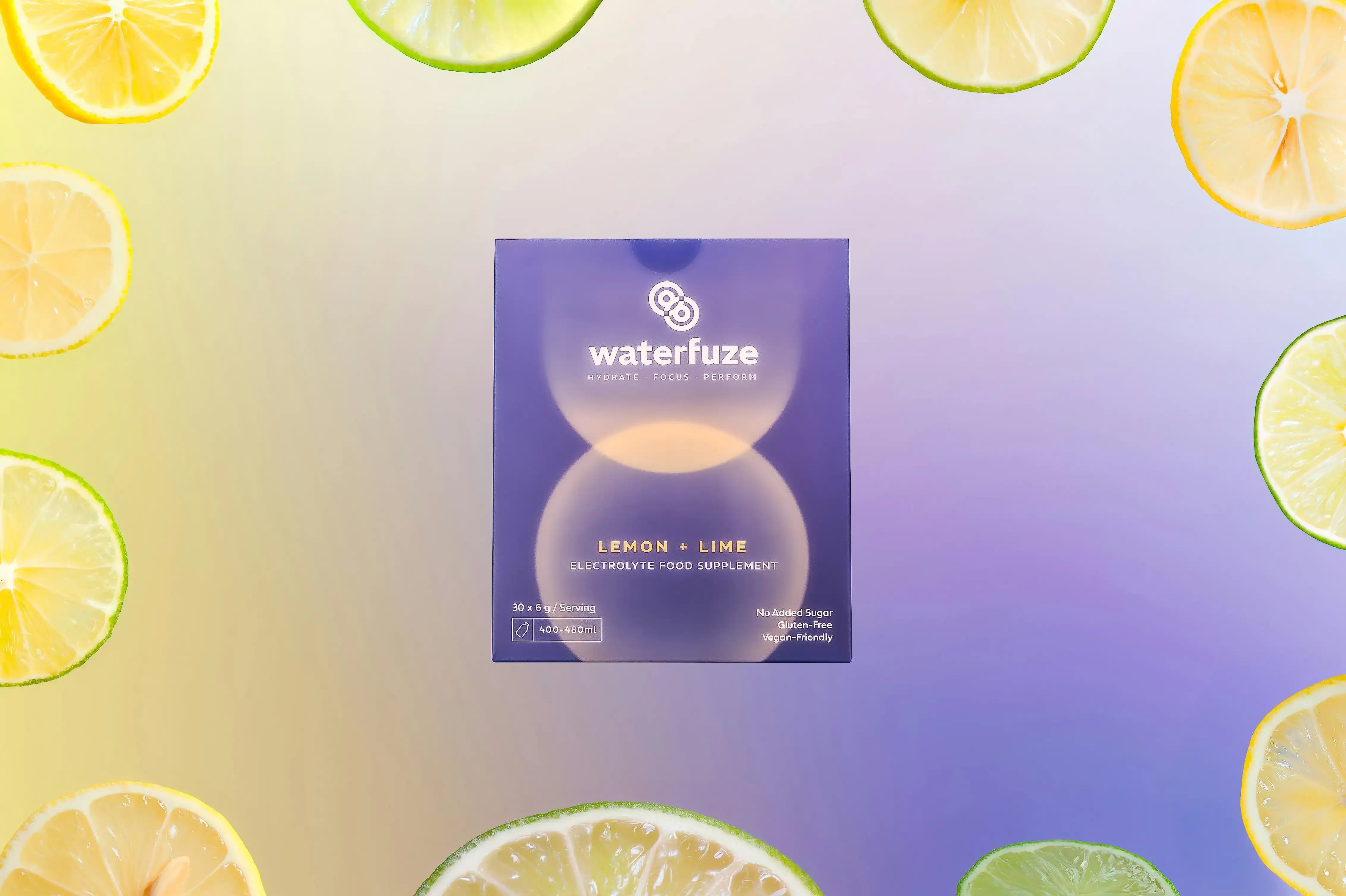 Waterfuze lemon-lime elektrolyten supplement doos omringd door plakjes citroen en limoen op kleurrijke achtergrond