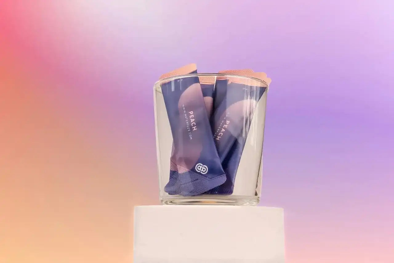 Glas gevuld met peach-flavored elektrolyten sticks tegen een pastel gekleurde achtergrond